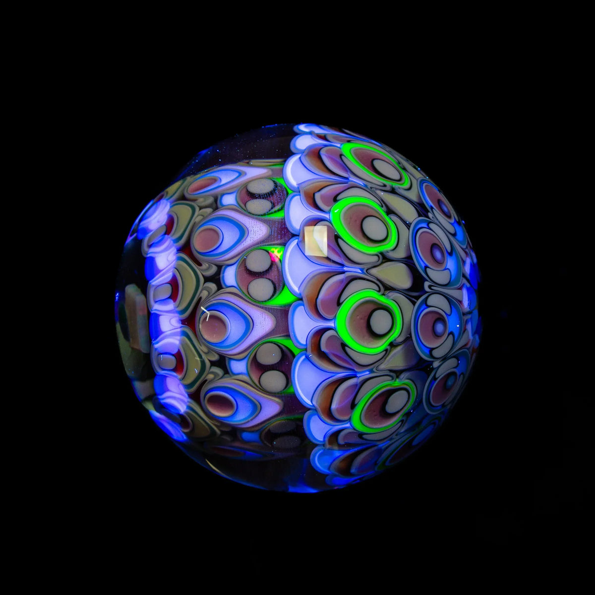 Handcrafted glass art marble with vibrant UV-reactive patterns on a black background