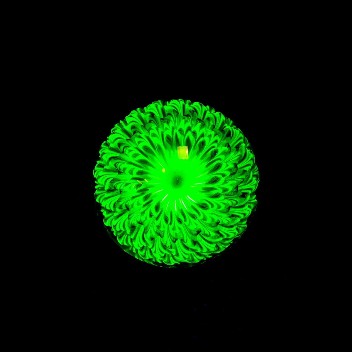 UV reactive green glass art sphere with intricate floral pattern on black background