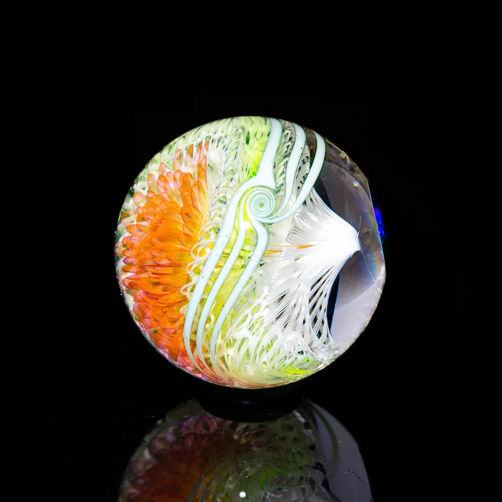 Heady glass marble with orange, green, and white swirling patterns on black background