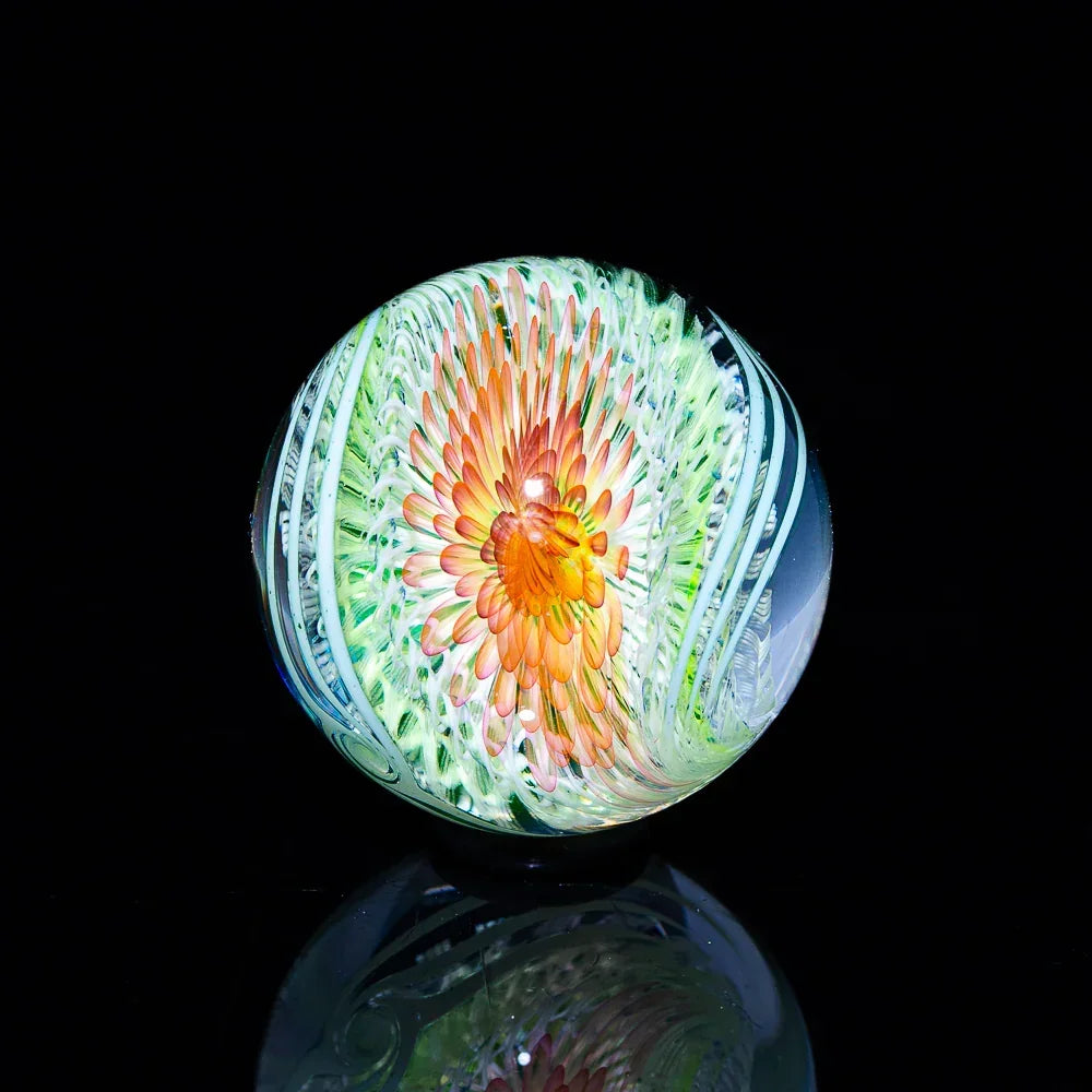 Handcrafted glass marble with vibrant orange and green flower design on black background