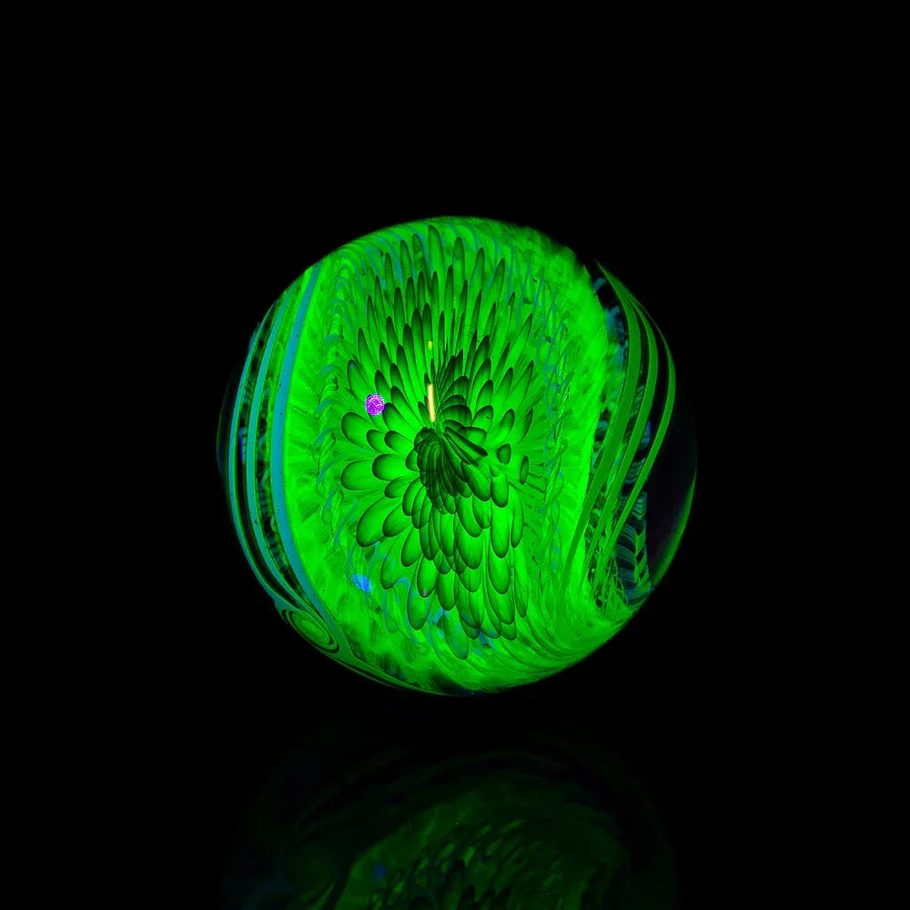 UV reactive green glass art marble with intricate swirling flower pattern on black background
