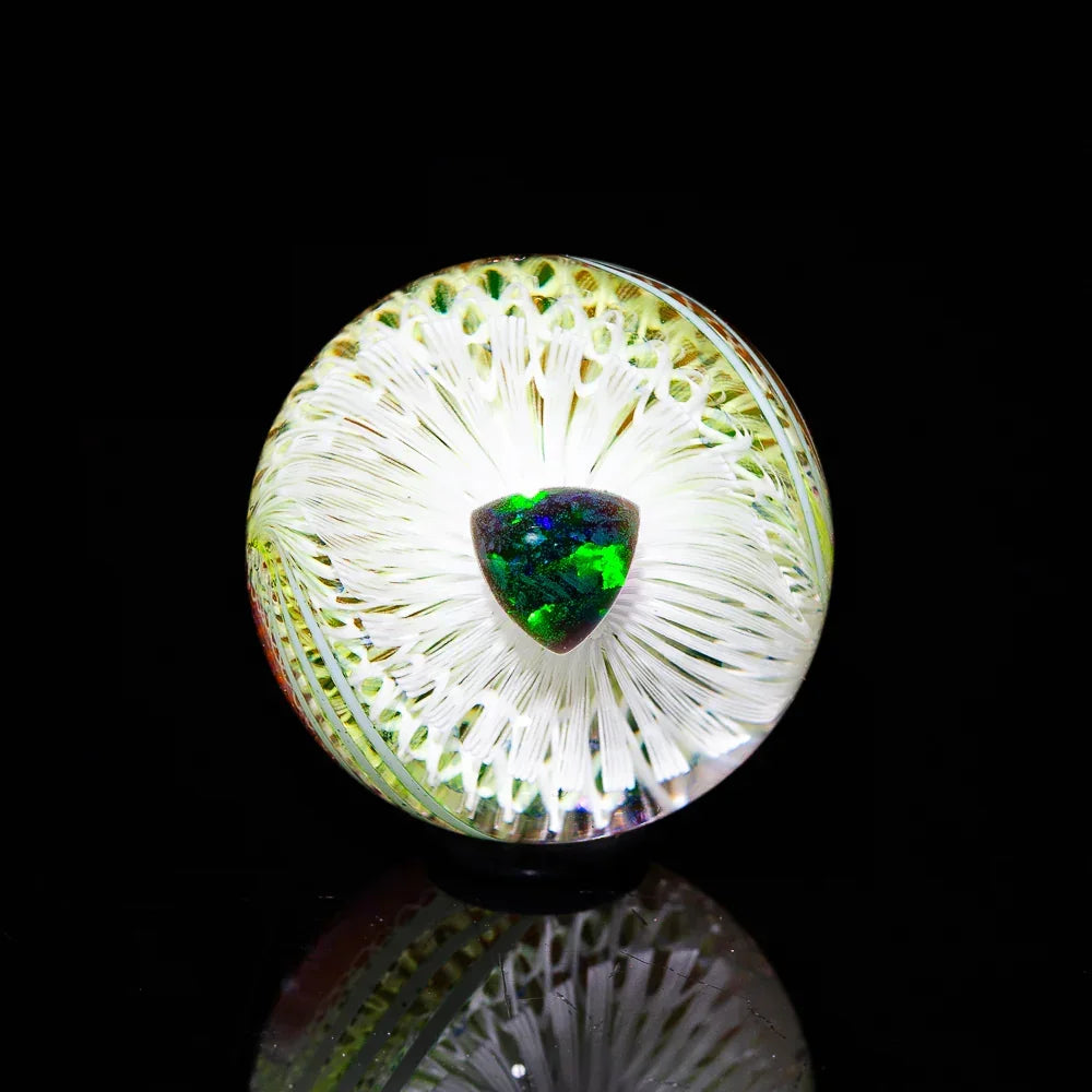 Heady glass marble with green opal core and intricate white fume designs on black background