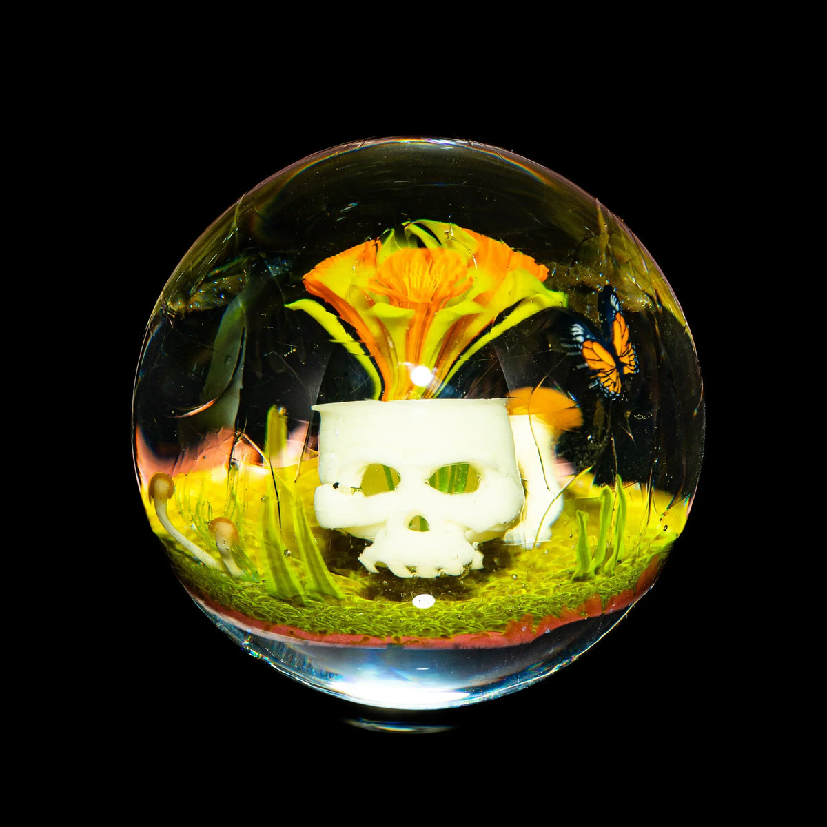 Glass art sphere with a white skull, yellow flower, butterfly, and green accents inside