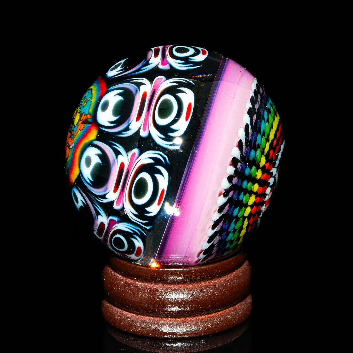 Colorful heady glass marble with psychedelic patterns on a wooden stand, black background.