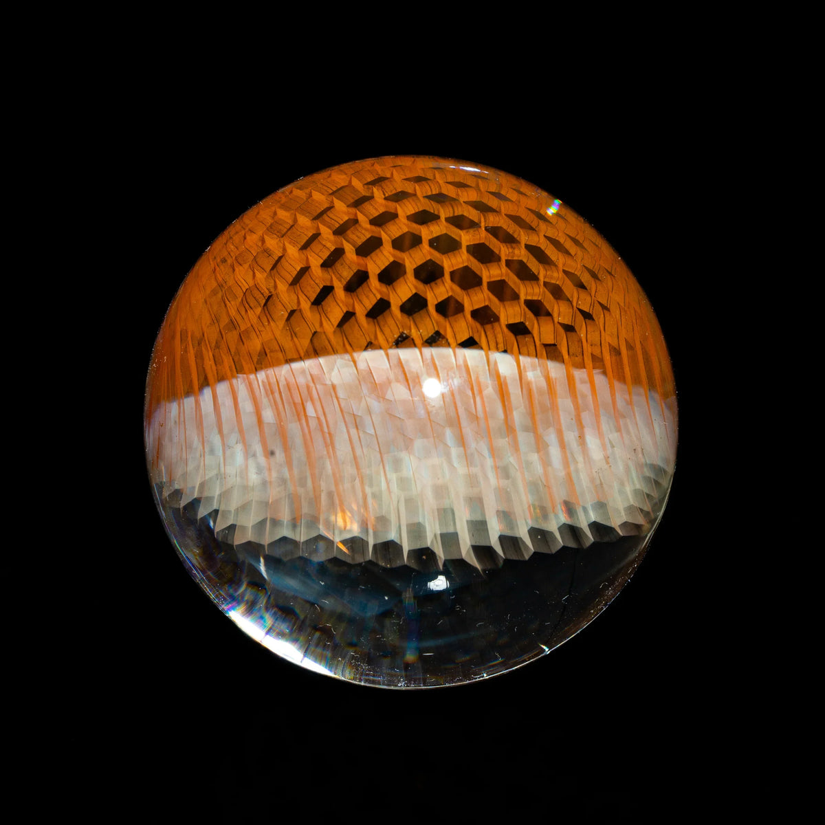 Handcrafted glass marble with honeycomb pattern and orange accents on black background