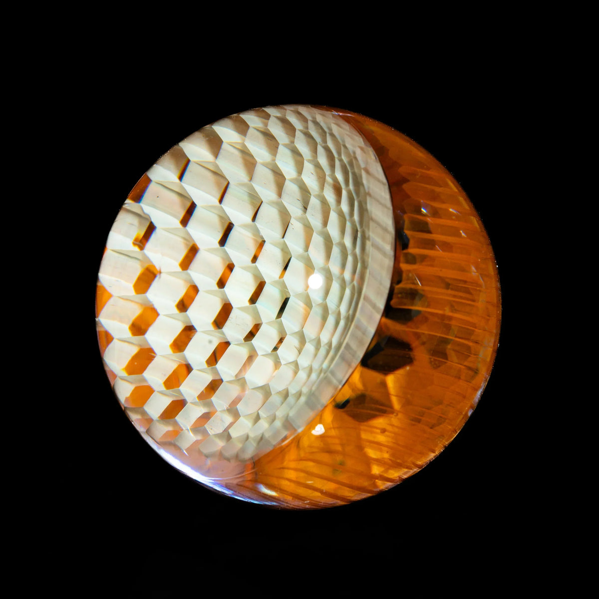 Close-up of a honeycomb-patterned glass marble with amber and clear sections on black background