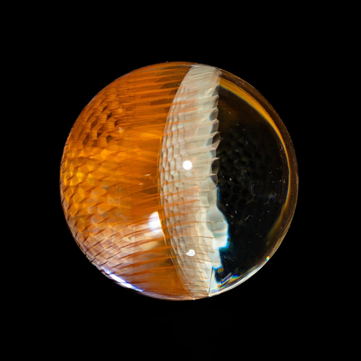 Close-up of a textured glass marble with orange and clear sections on a black background