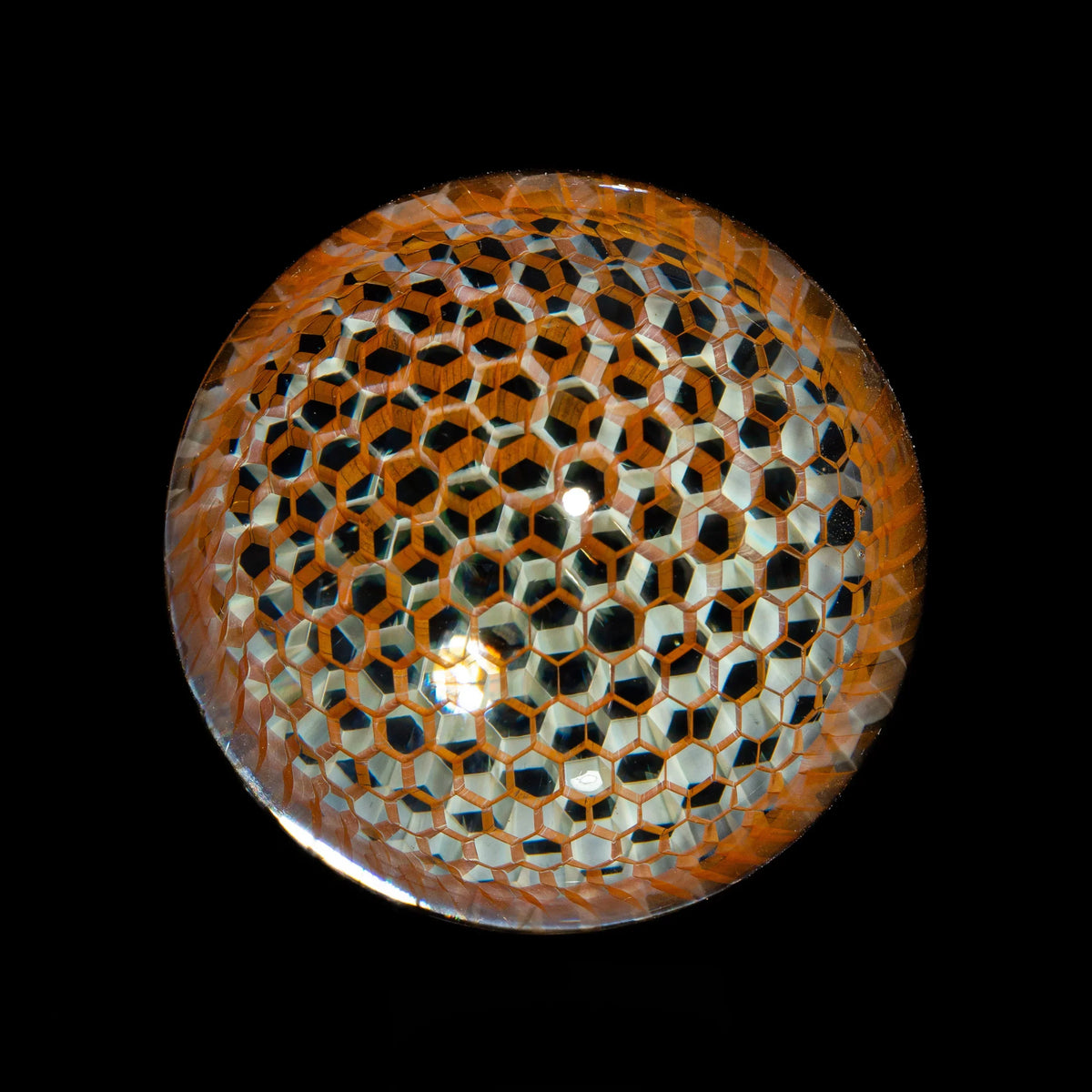 Handcrafted glass marble with orange and black honeycomb pattern, isolated on black background