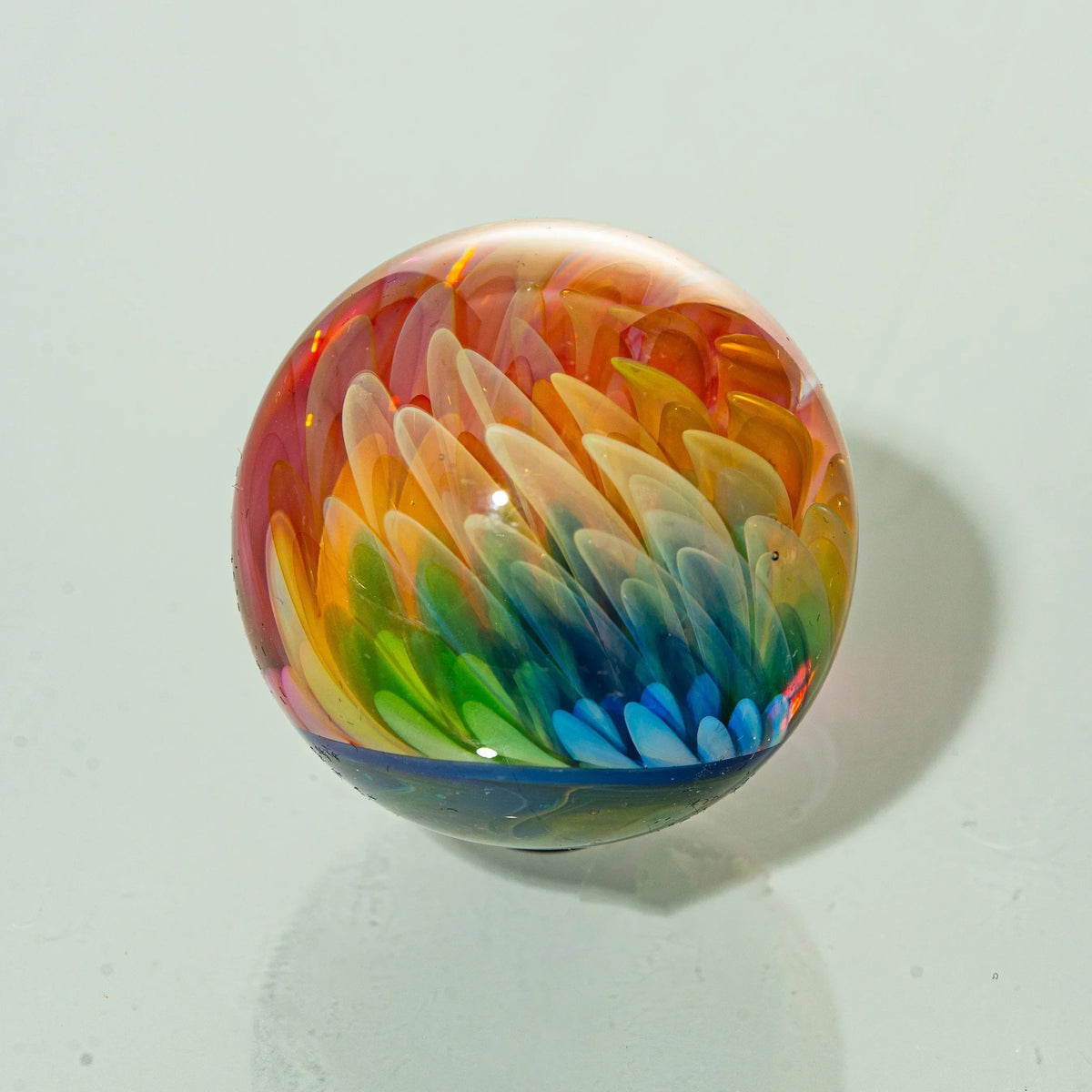 Handcrafted glass marble with intricate rainbow feather design