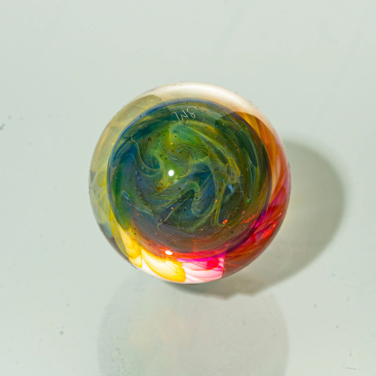 Colorful hand-blown glass marble with swirling patterns on a white background