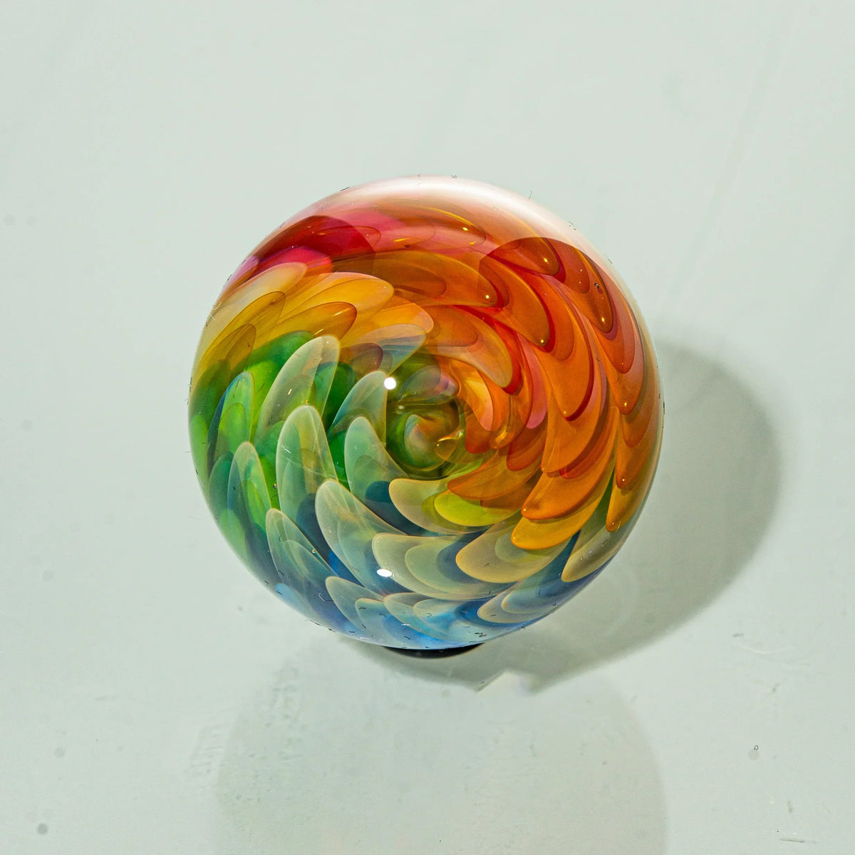 Colorful hand-blown glass marble with rainbow swirl pattern on light background