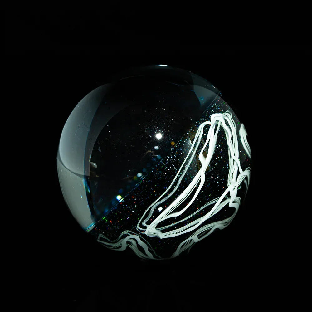 Handcrafted glass marble with white line art and sparkling detail on a black background