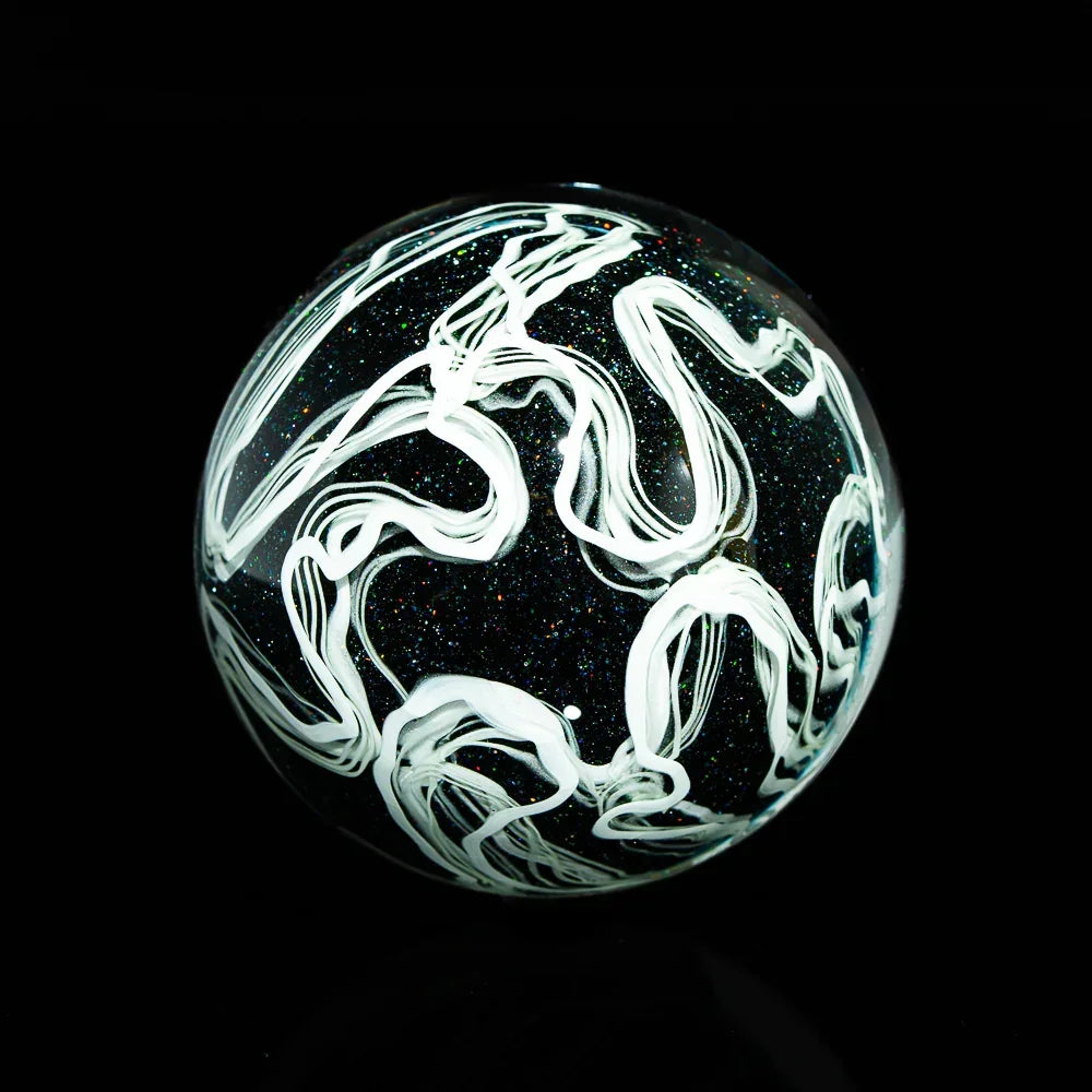 Handcrafted glass marble with white swirl patterns on a black, sparkly background