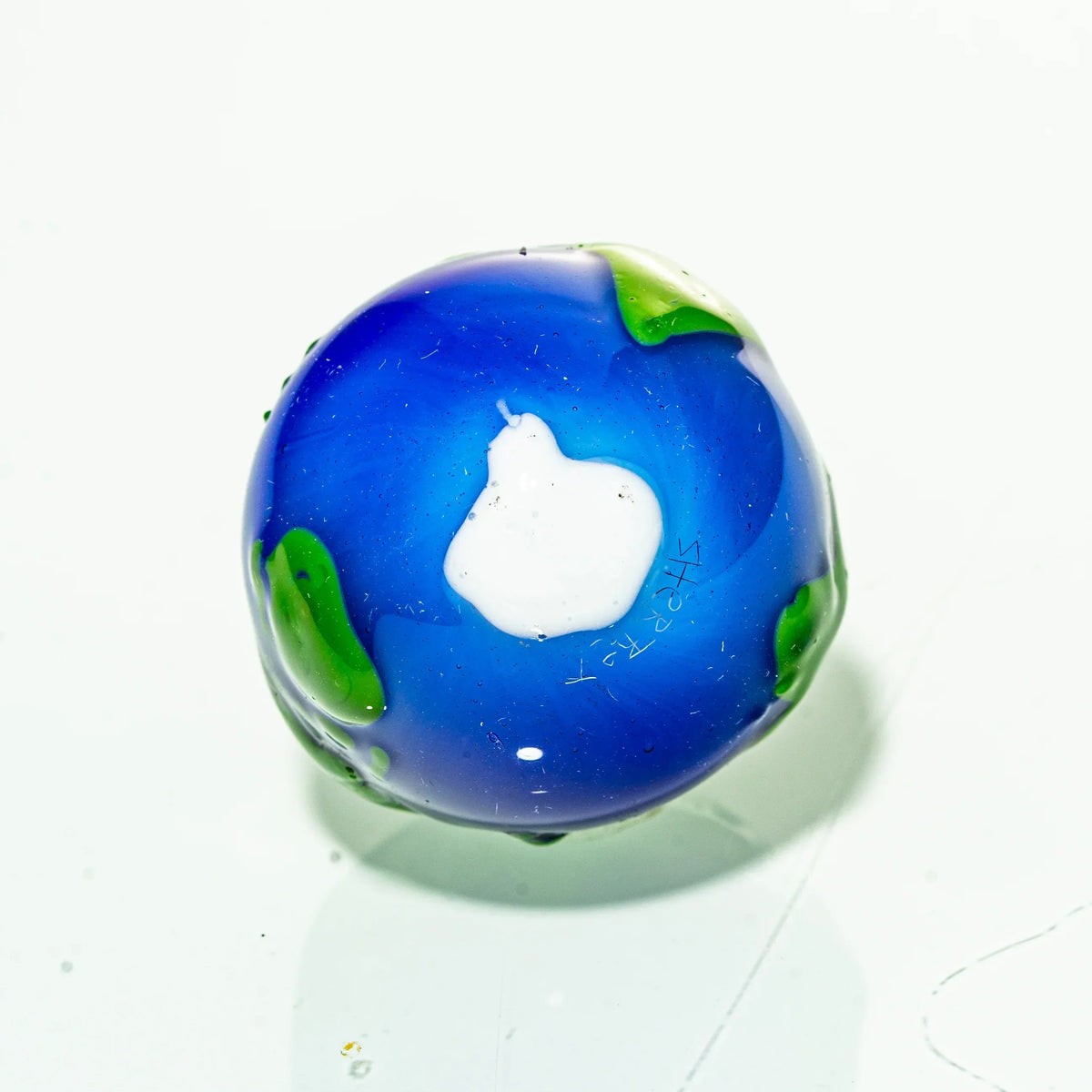 Handcrafted glass marble with blue, green, and white earth design on white background