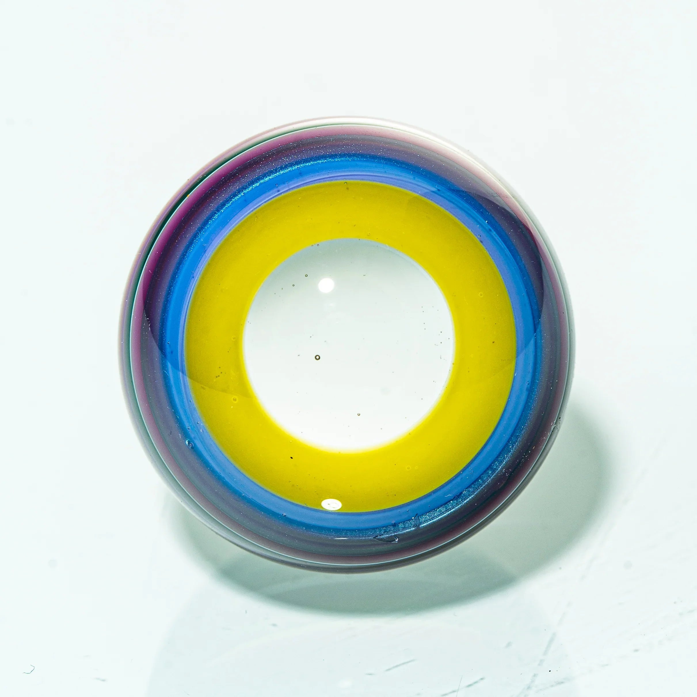 Colorful glass marble with yellow, blue, and purple rings on a white background