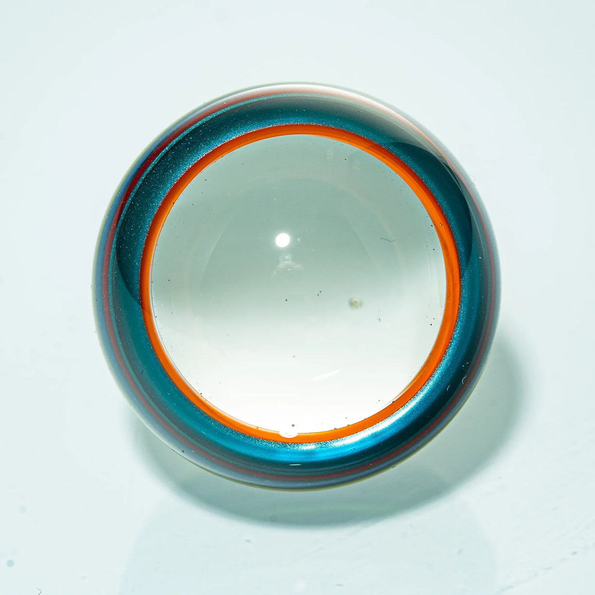Glass marble with clear center, blue and orange swirled rim on white background