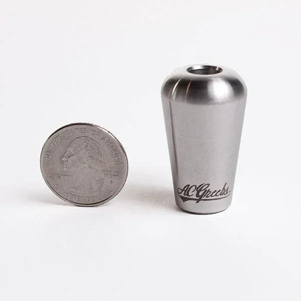 Stainless steel smoking pipe bowl with engraved logo next to a US quarter for size comparison.