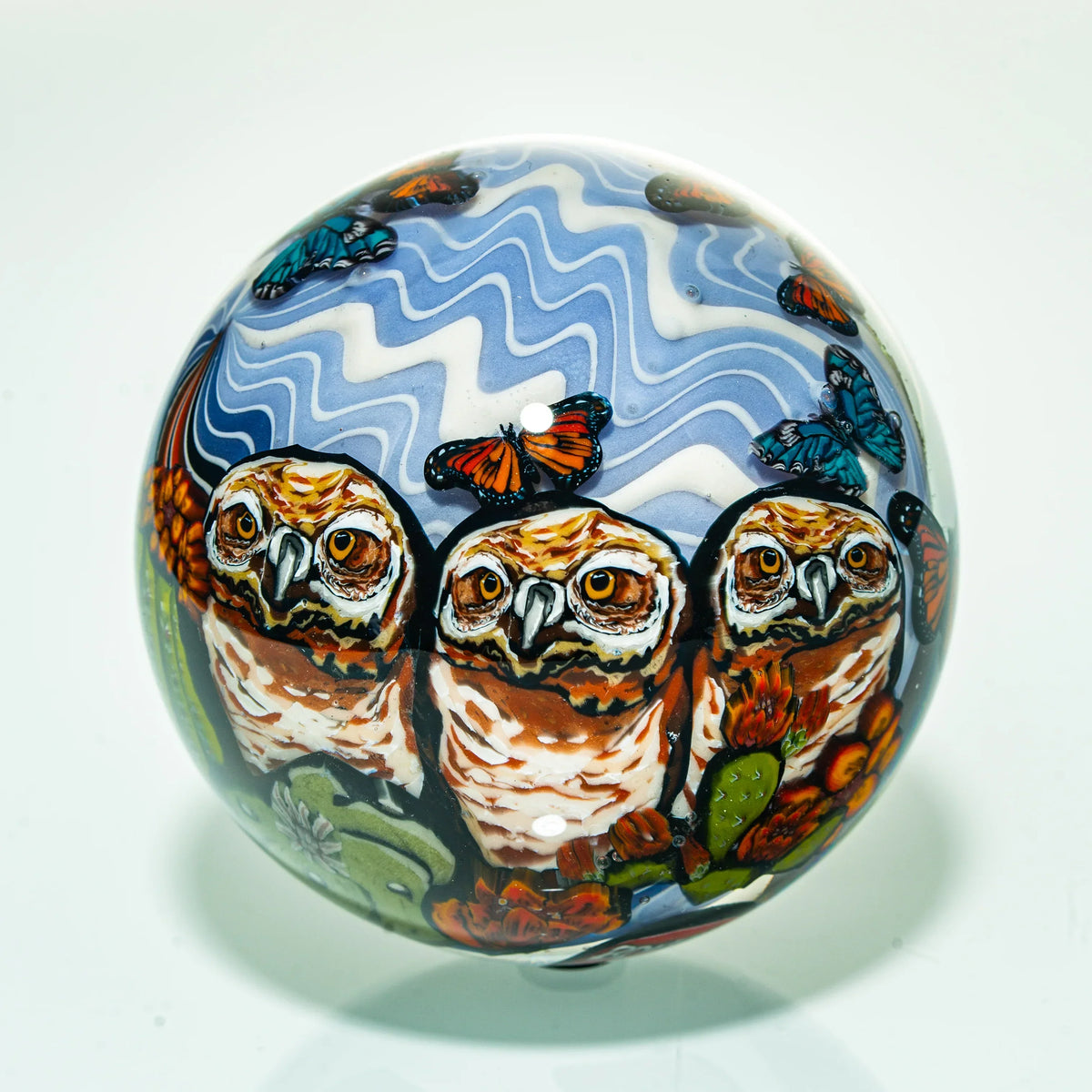 Handcrafted glass art sphere featuring three owls, butterflies, and blue wavy patterns