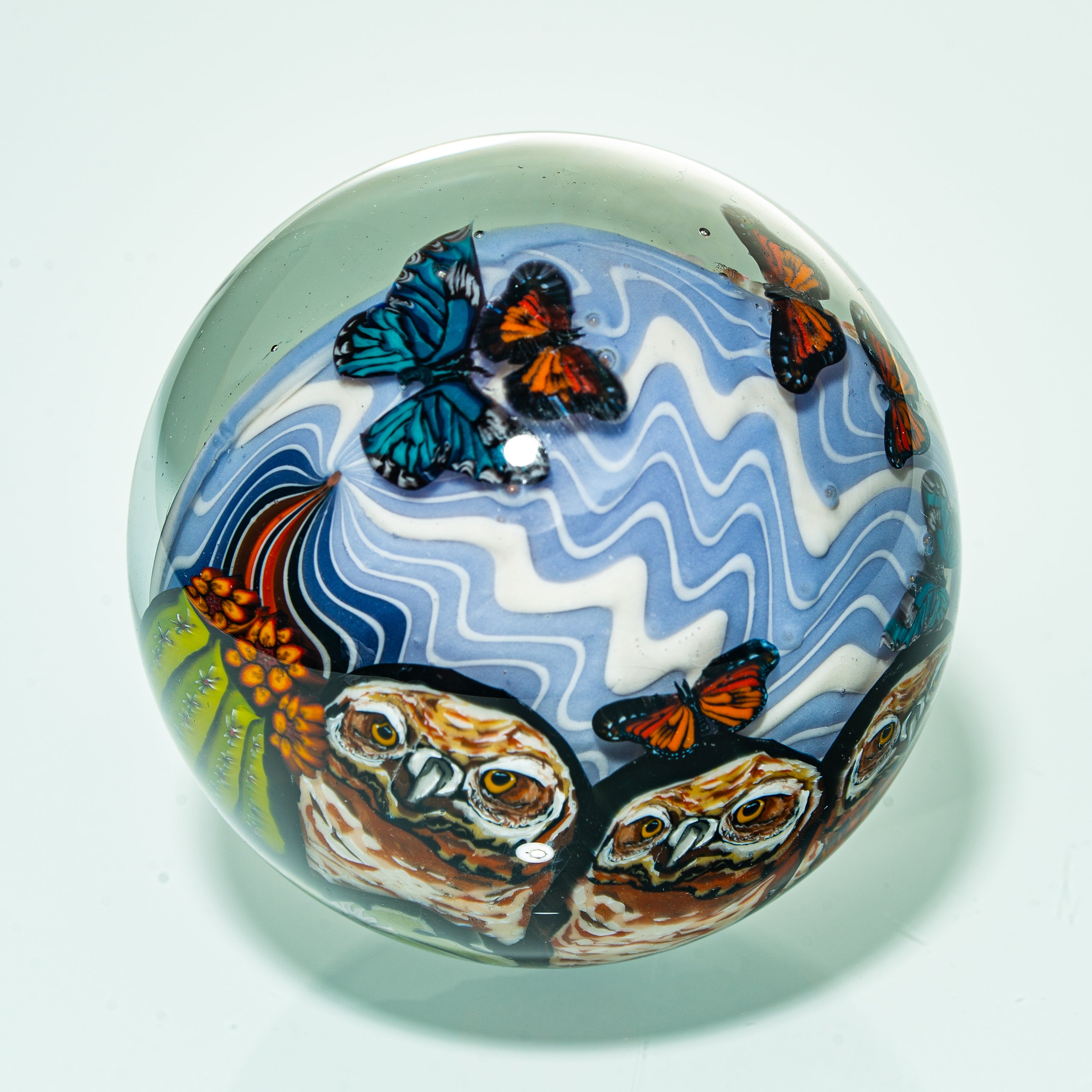 Hand-blown glass ball featuring owl faces, blue butterflies, and wavy patterns