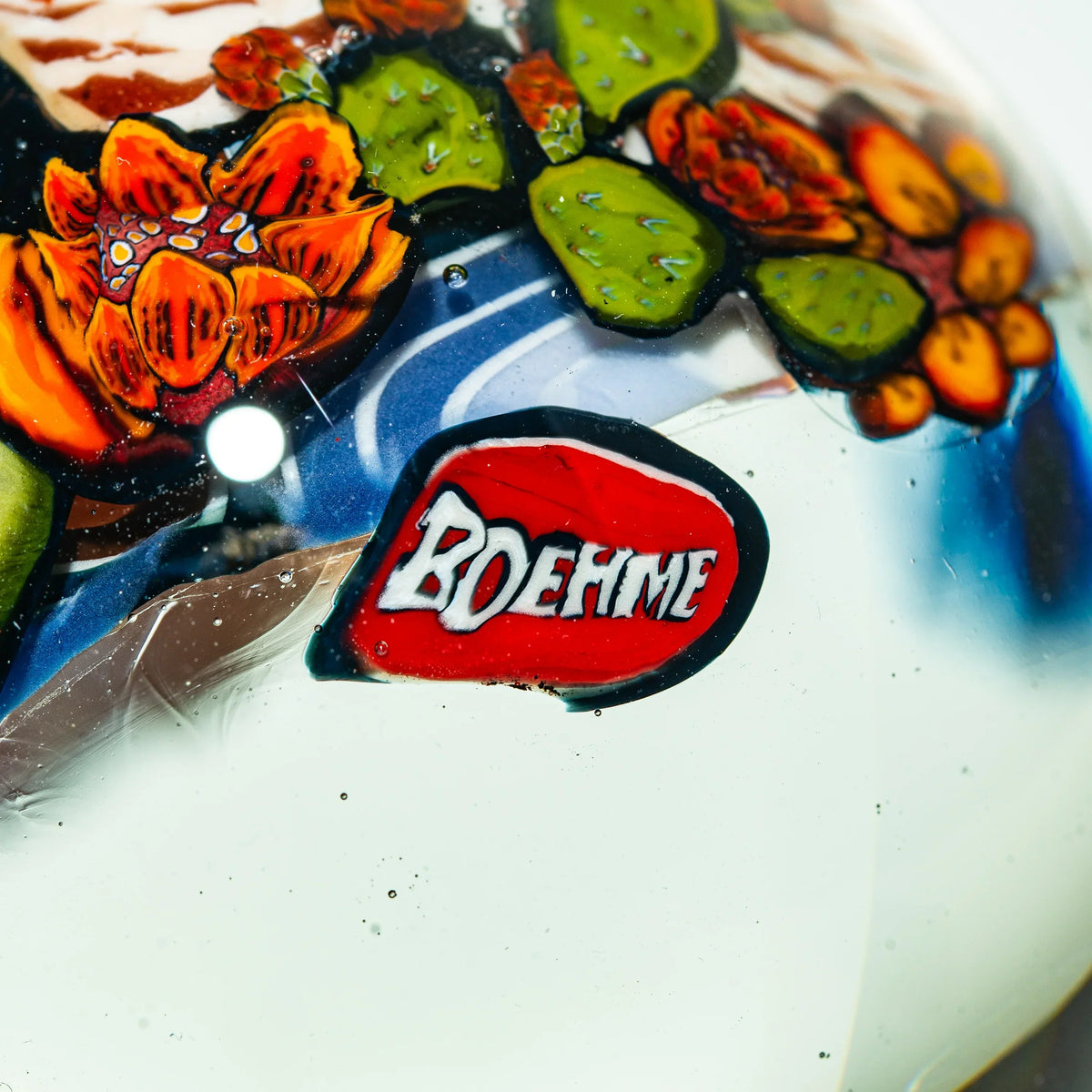 Close-up of intricate glass art with orange flower, green cactus, and Boehme signature detail