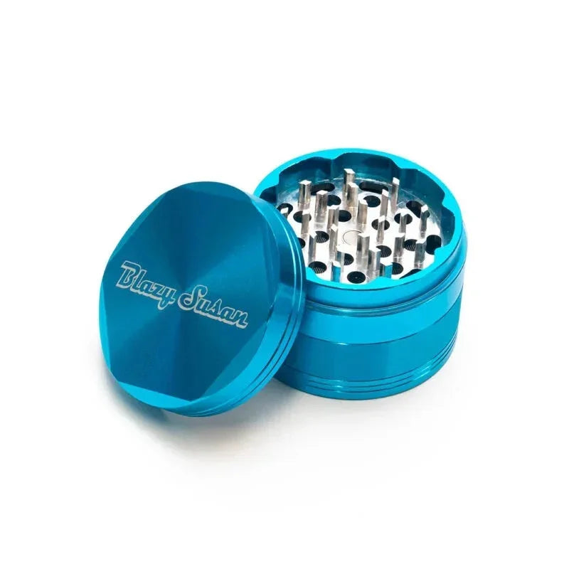 Teal aluminum herb grinder with open lid and sharp grinding teeth, Blazy Susan logo visible.