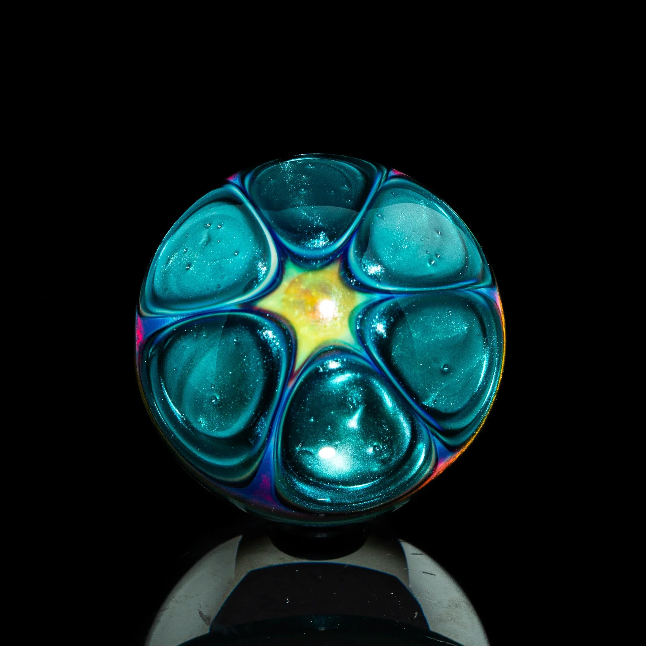 Iridescent teal glass marble with starburst pattern on black background