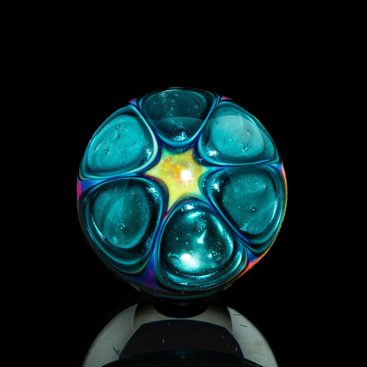 Iridescent teal glass marble with starburst pattern on black background