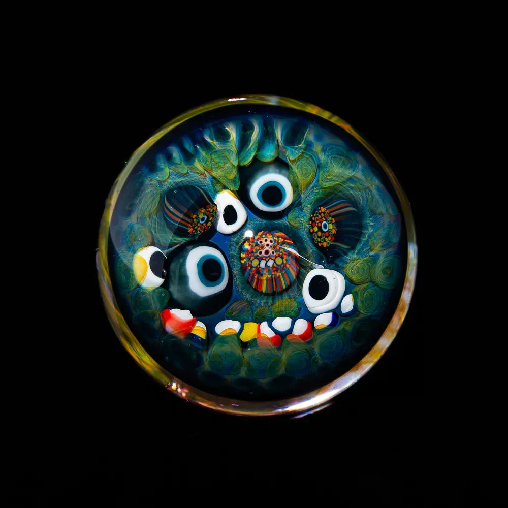 Colorful blown glass marble with abstract monster face design on black background
