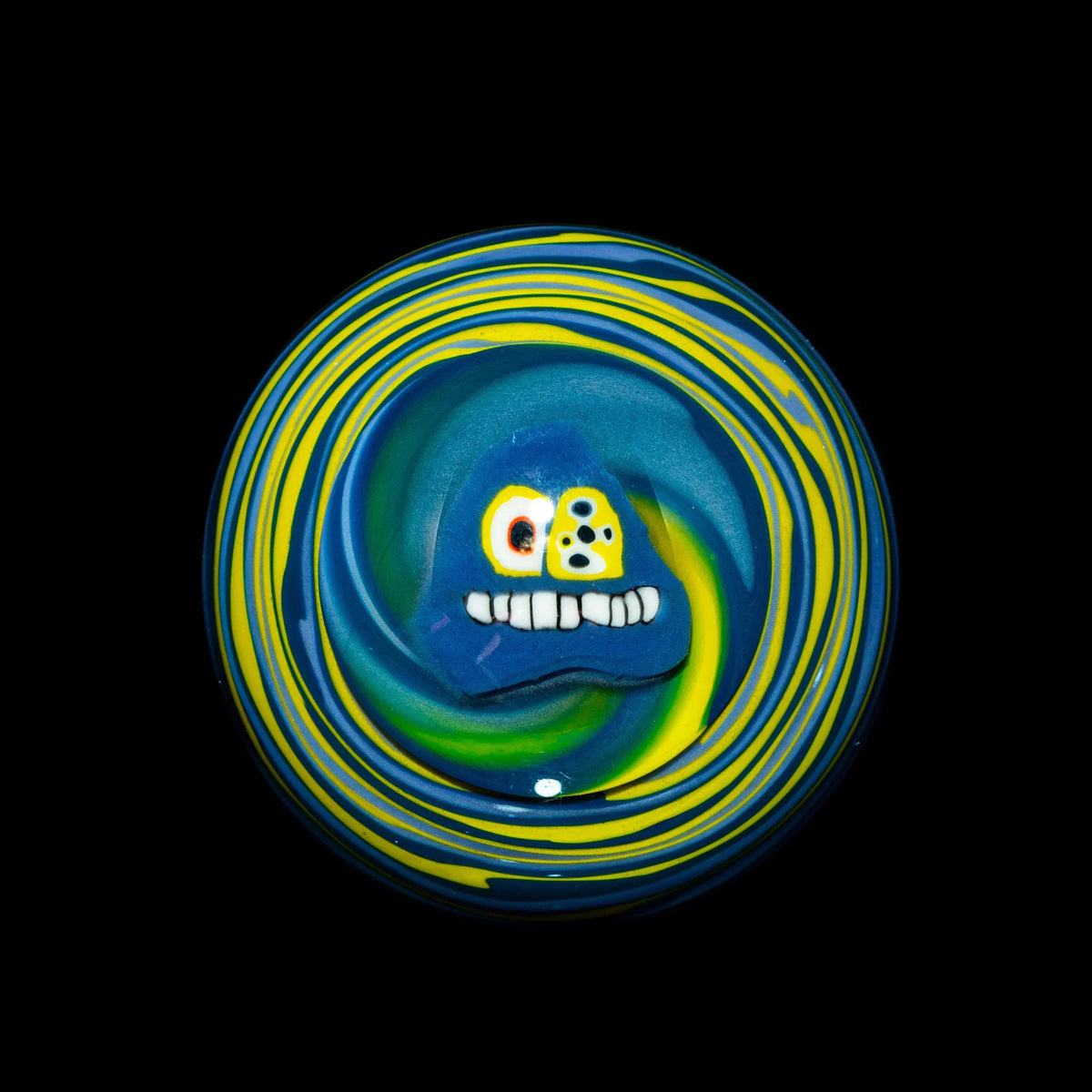 Colorful heady glass carb cap with blue, yellow, and green swirls and a cartoon face