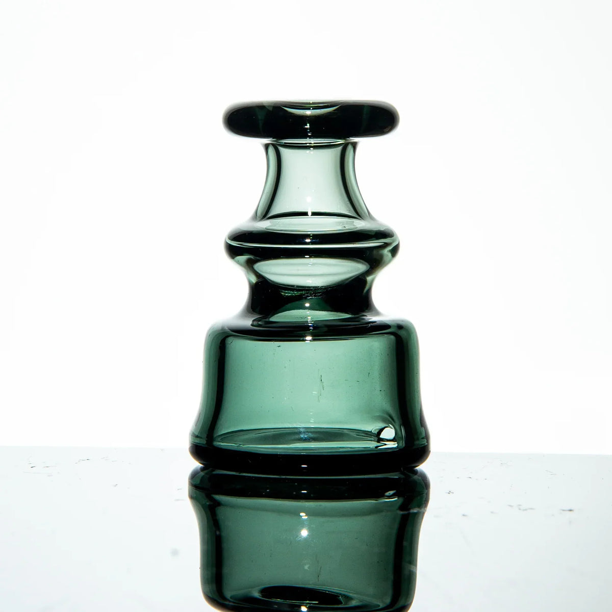 Thick green glass carb cap for dab rigs with a reflective surface background
