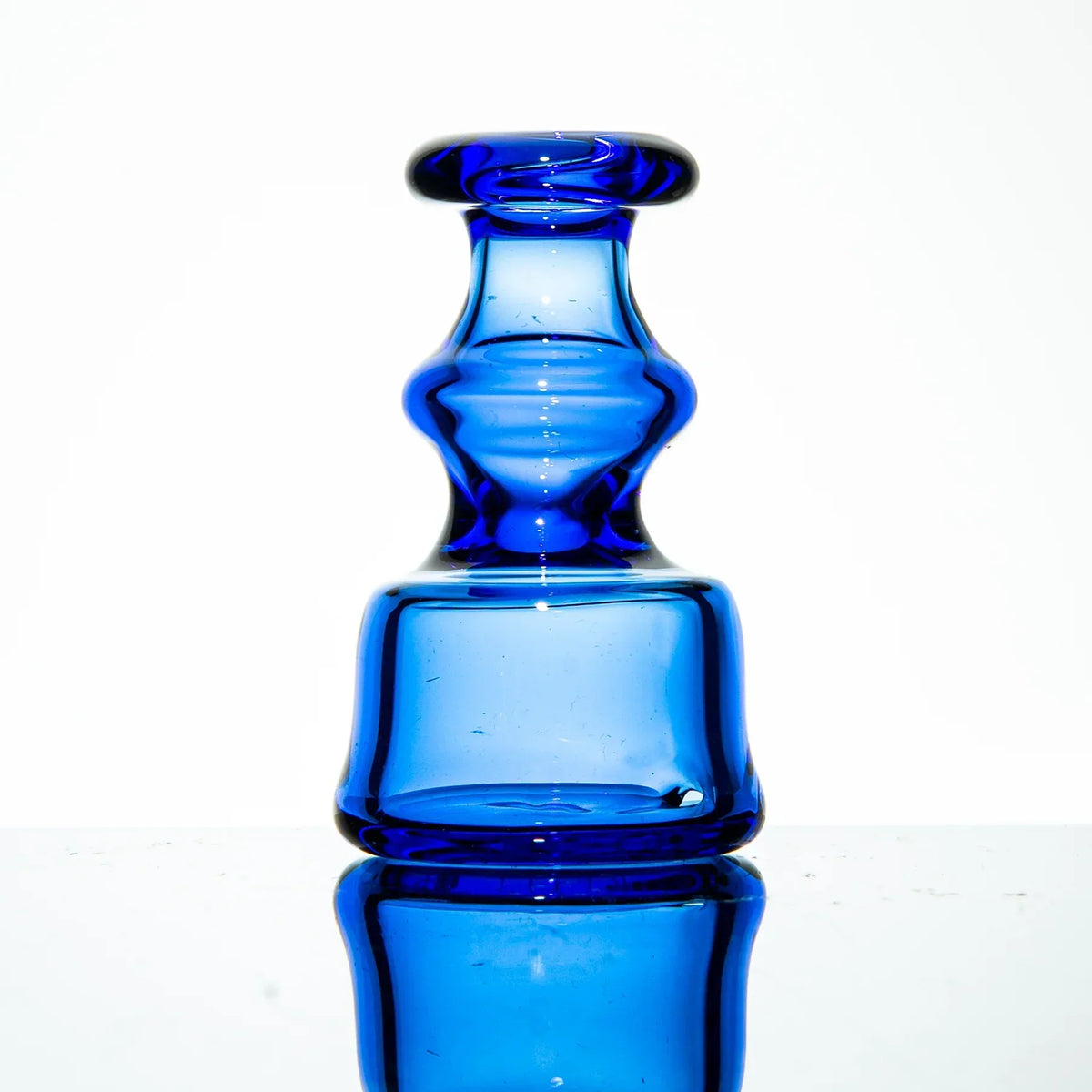 Cobalt blue glass carb cap accessory with unique contours on a mirrored surface