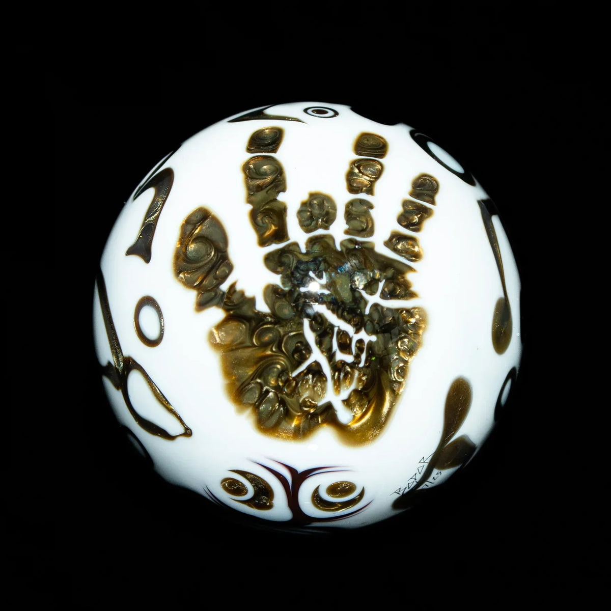 White glass marble with intricate gold handprint and patterned designs on black background