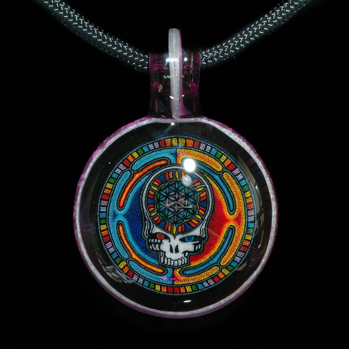 Colorful glass pendant with psychedelic skull design on braided cord, black background
