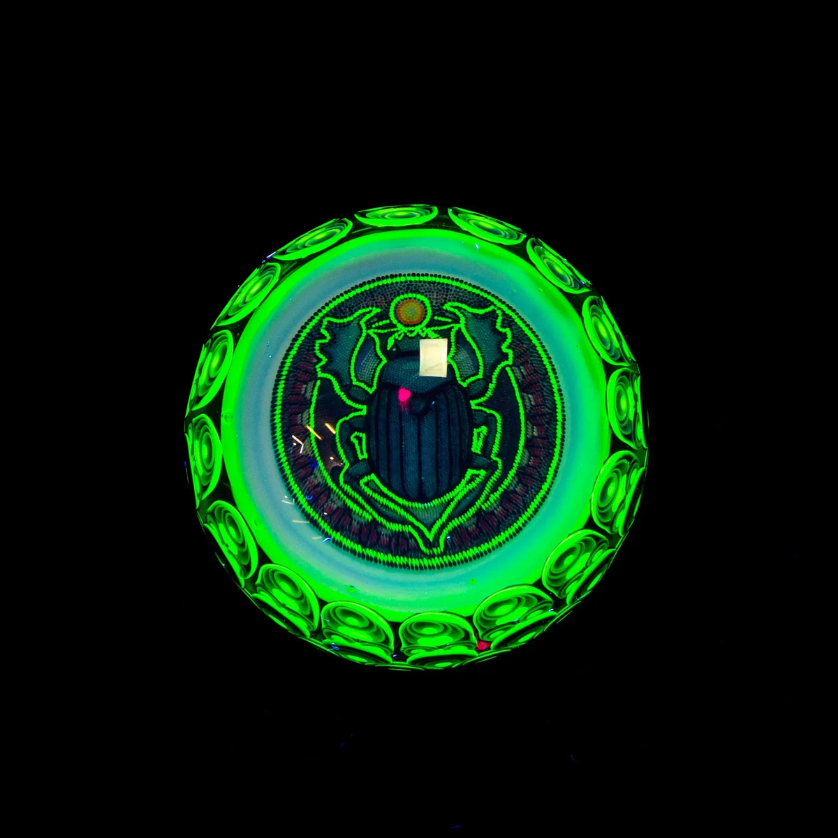 UV-reactive glass art pendant with neon green scarab beetle design on black background