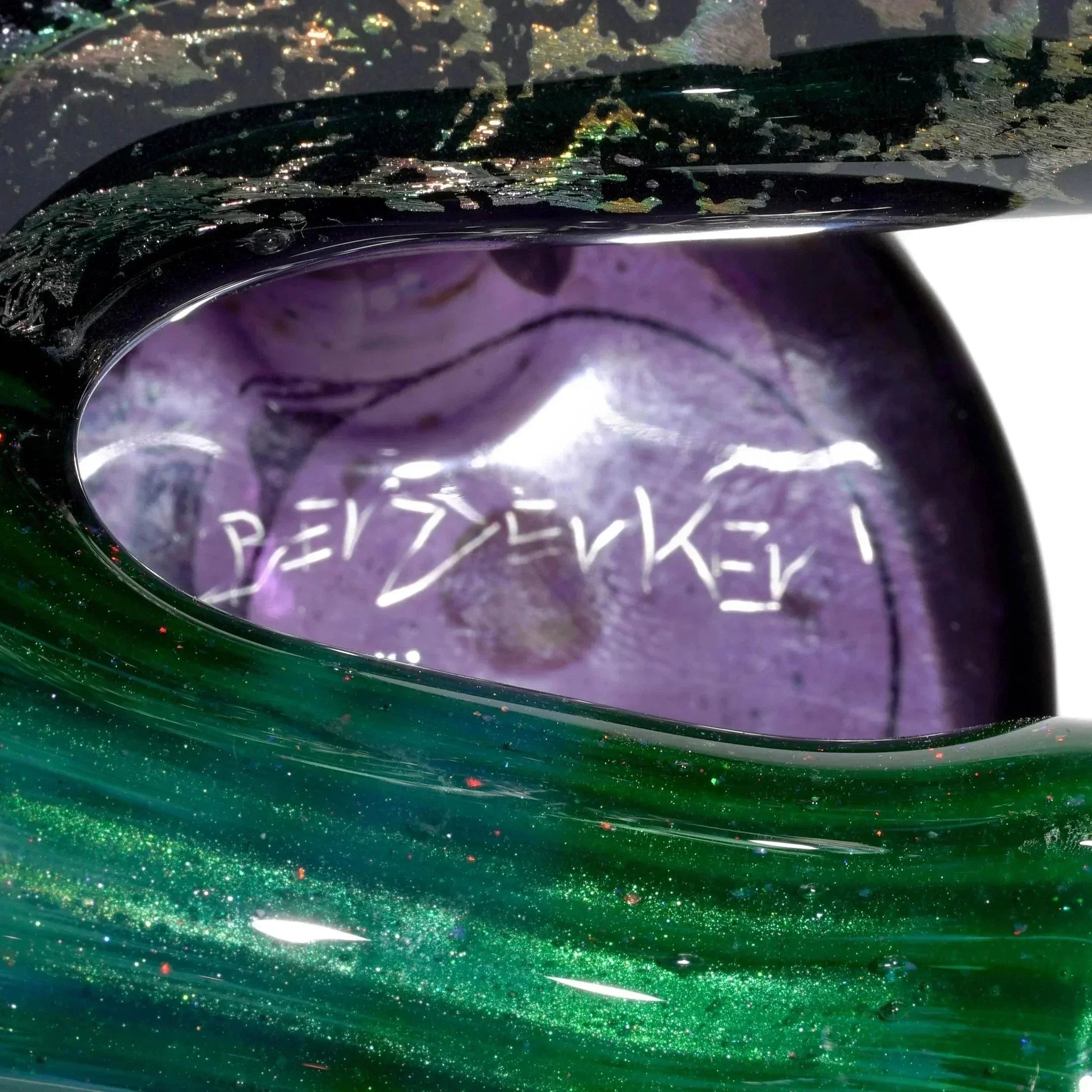 Close-up of iridescent green and purple heady glass art pipe with artist signature.