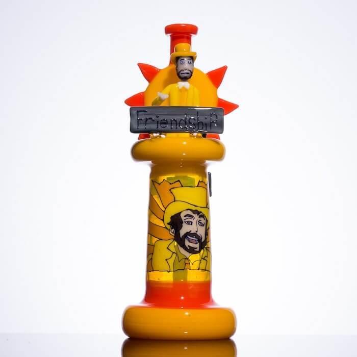 Vibrant yellow and orange glass pipe with cartoon character, sunburst design, and 'Friendship' sign