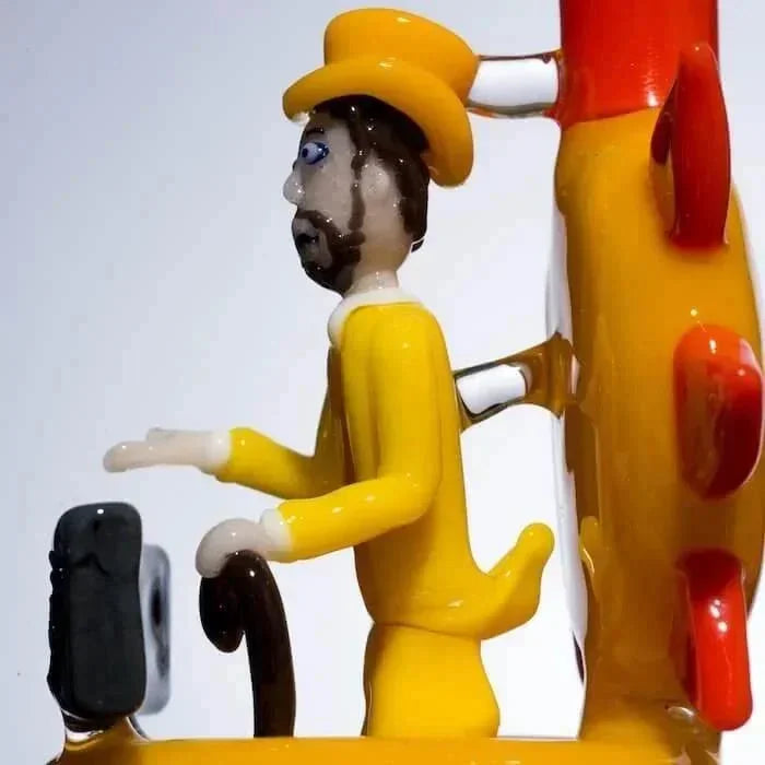 Yellow glass figurine of man in hat playing piano, heady glass art piece