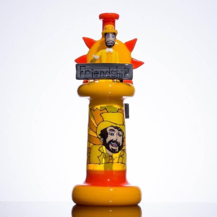 Vibrant yellow and orange glass pipe with cartoon character and 'Friendship' sign, heady glass art