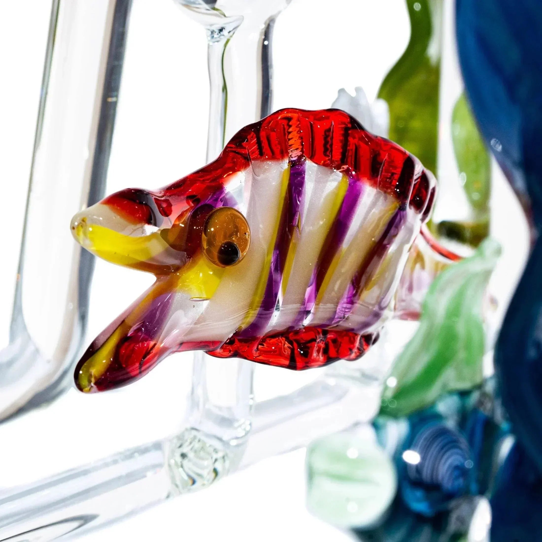 Colorful blown glass fish sculpture with red, yellow, and purple details on clear glass