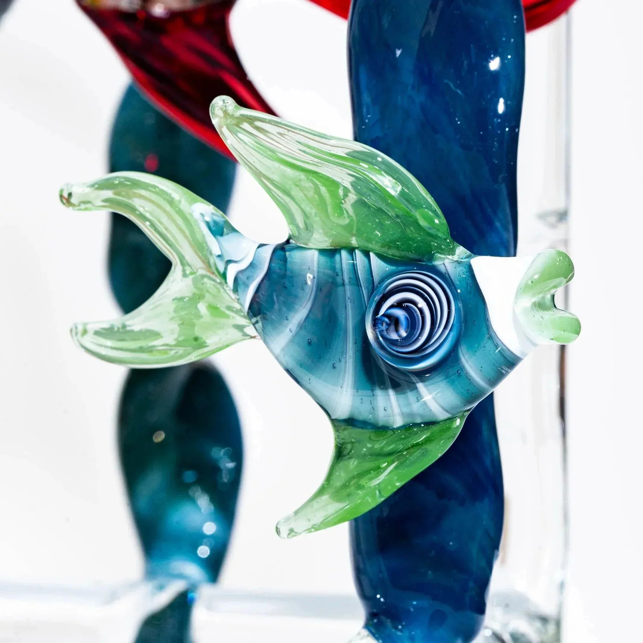 Colorful glass fish sculpture with green fins and blue swirled body on clear stand