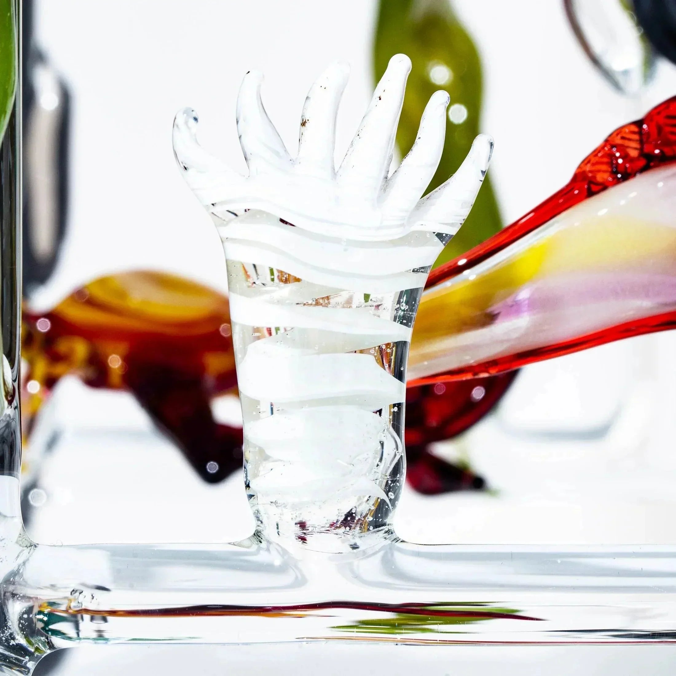 Hand-shaped clear and white glass sculpture with colorful glass accents in background