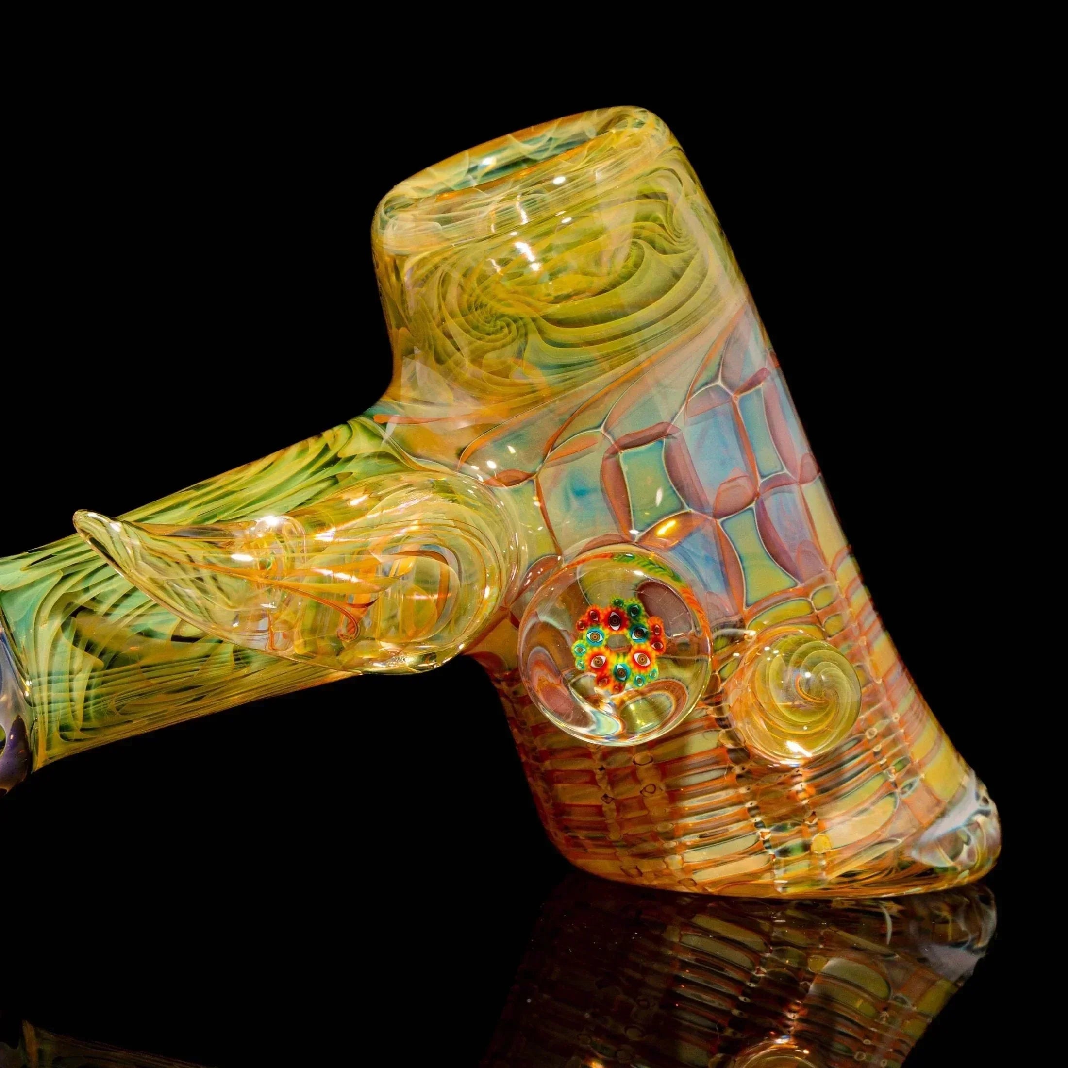 Heady glass hand pipe with intricate yellow, green, and orange patterns on a black background