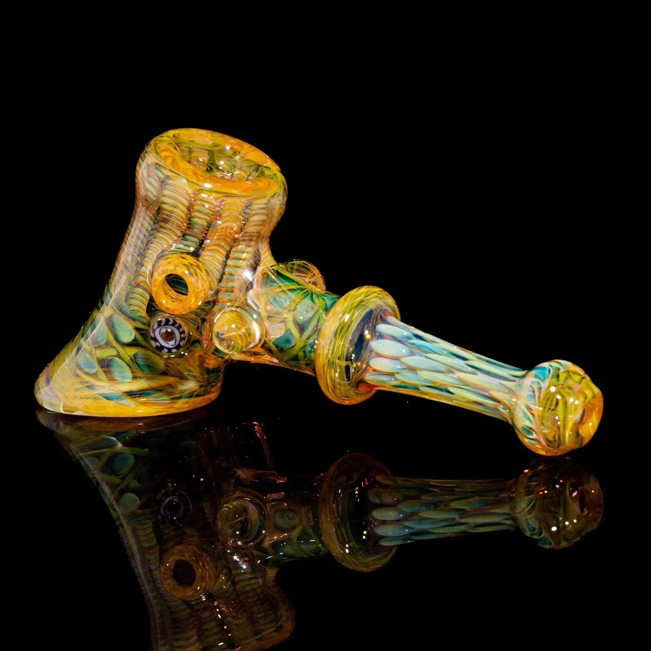Heady glass hand pipe with yellow, green, and blue patterns on black background