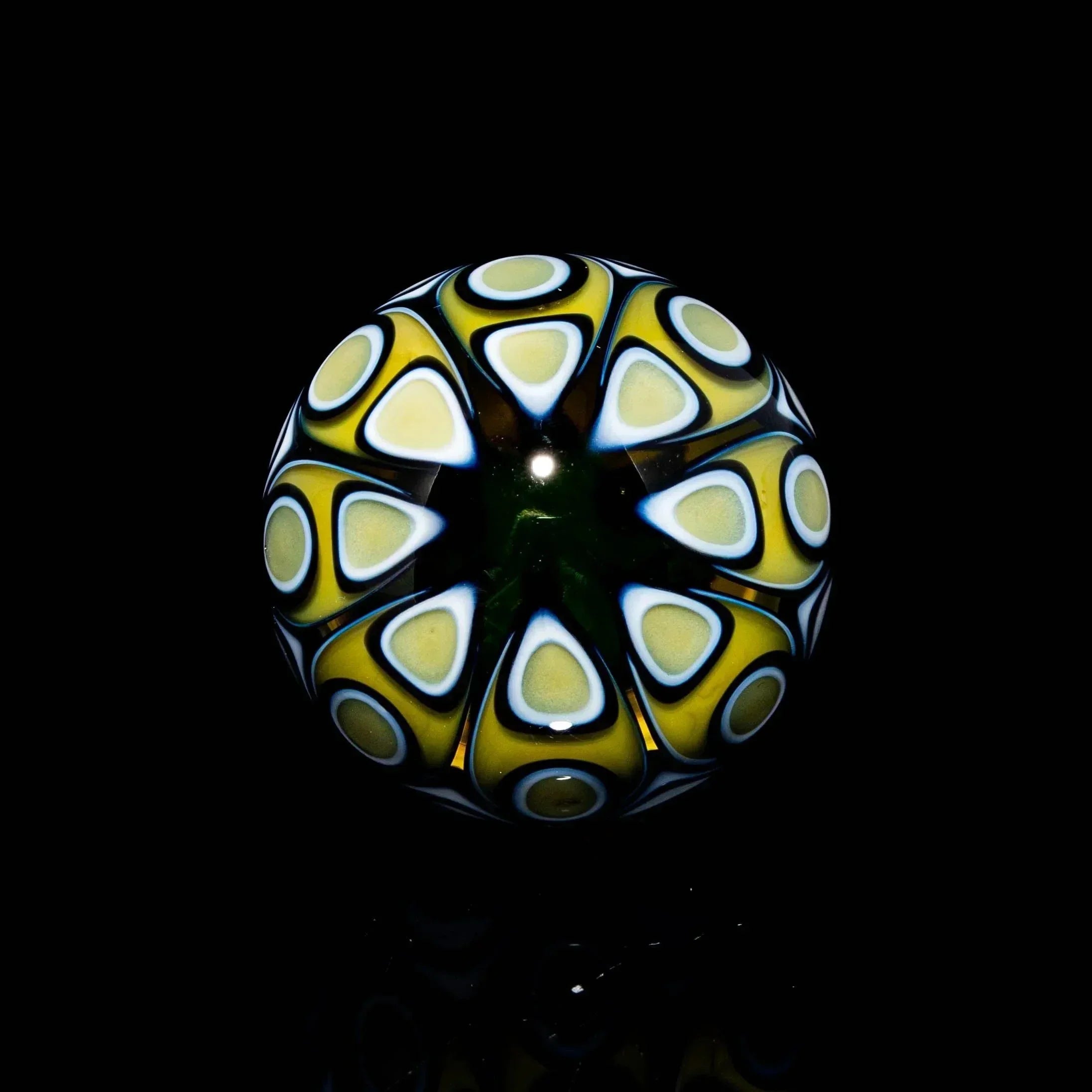 Hand-blown glass marble with yellow, white, and black geometric pattern on black background