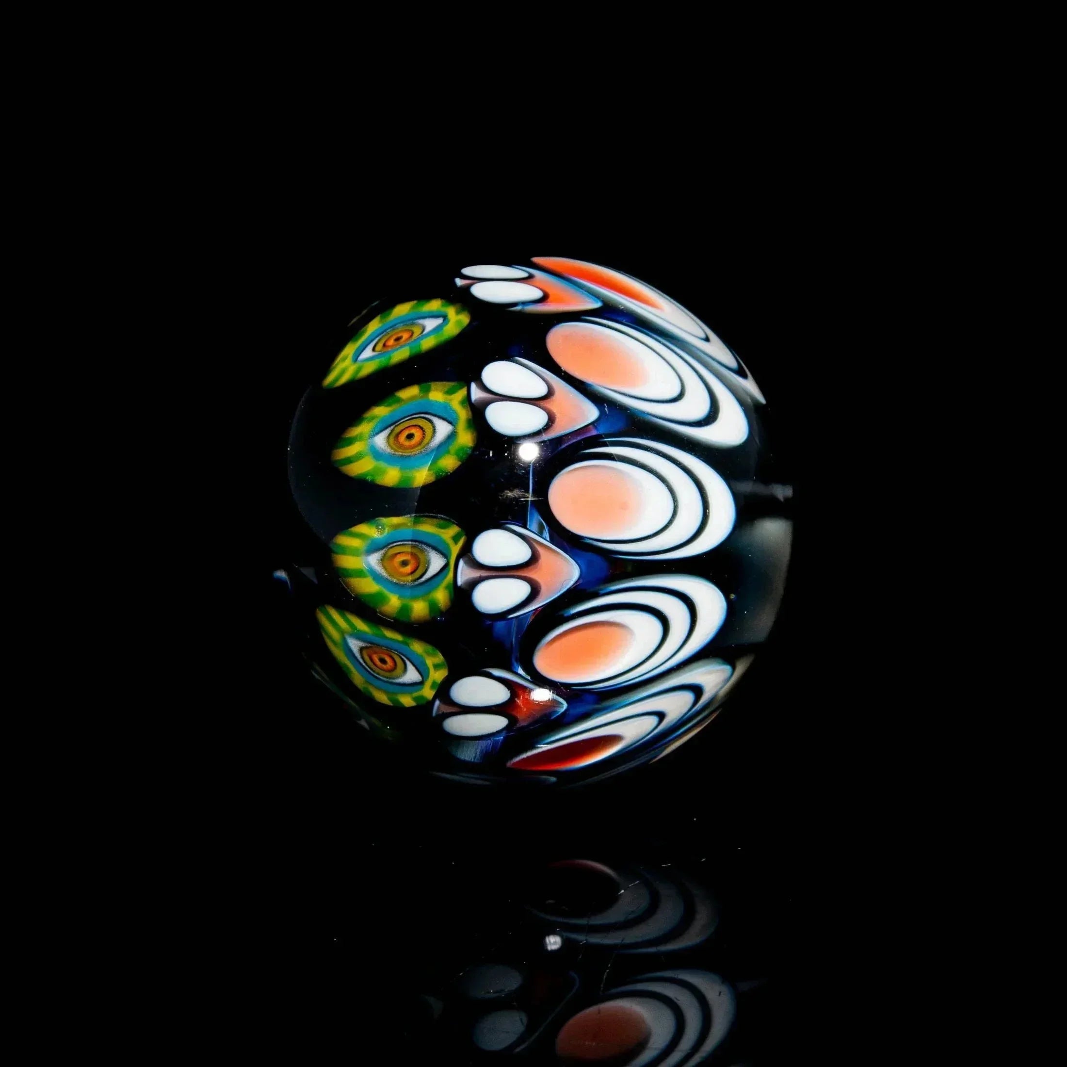 Hand-blown glass marble with colorful, intricate patterns on a black reflective surface