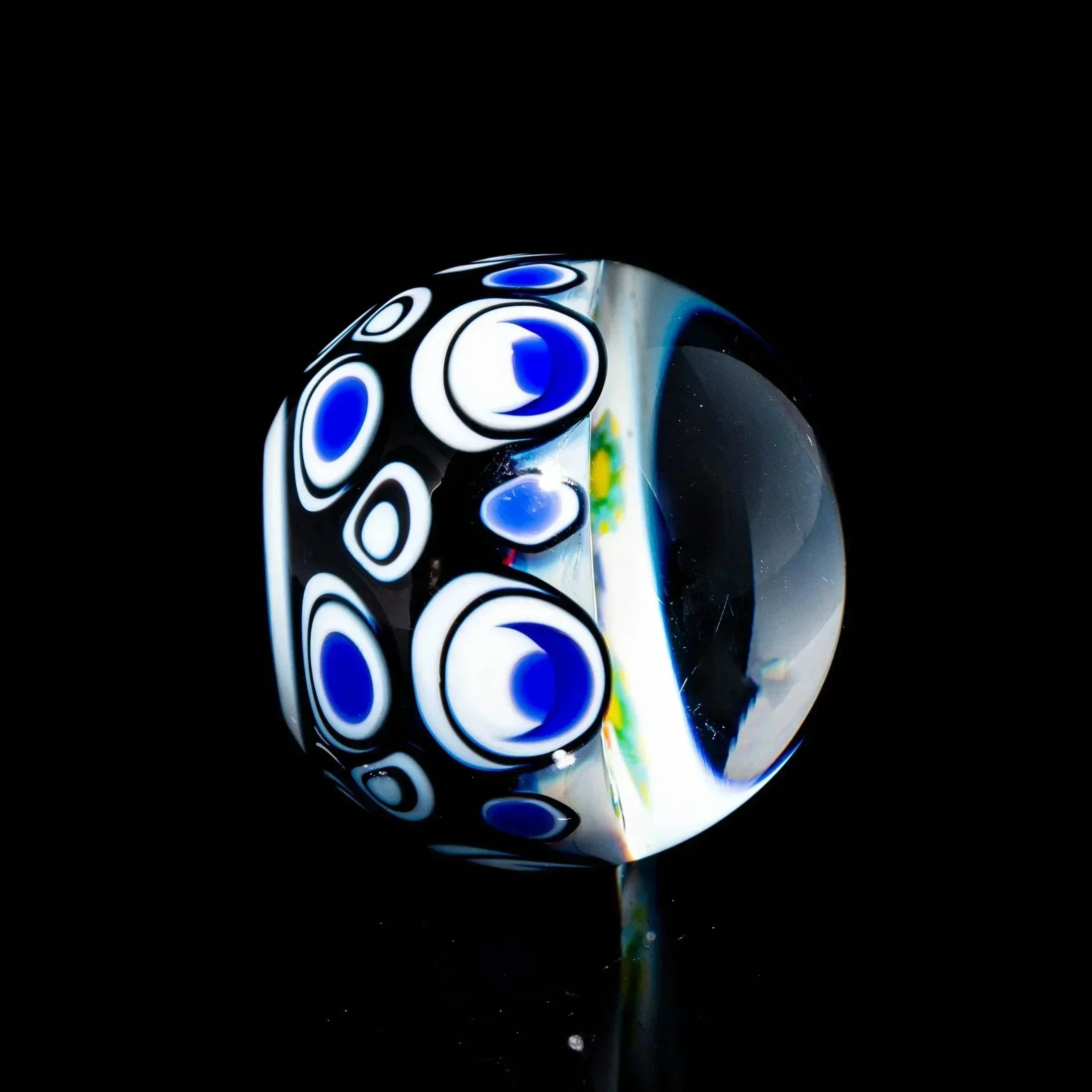 Handcrafted glass marble with blue and white eye pattern on a black background