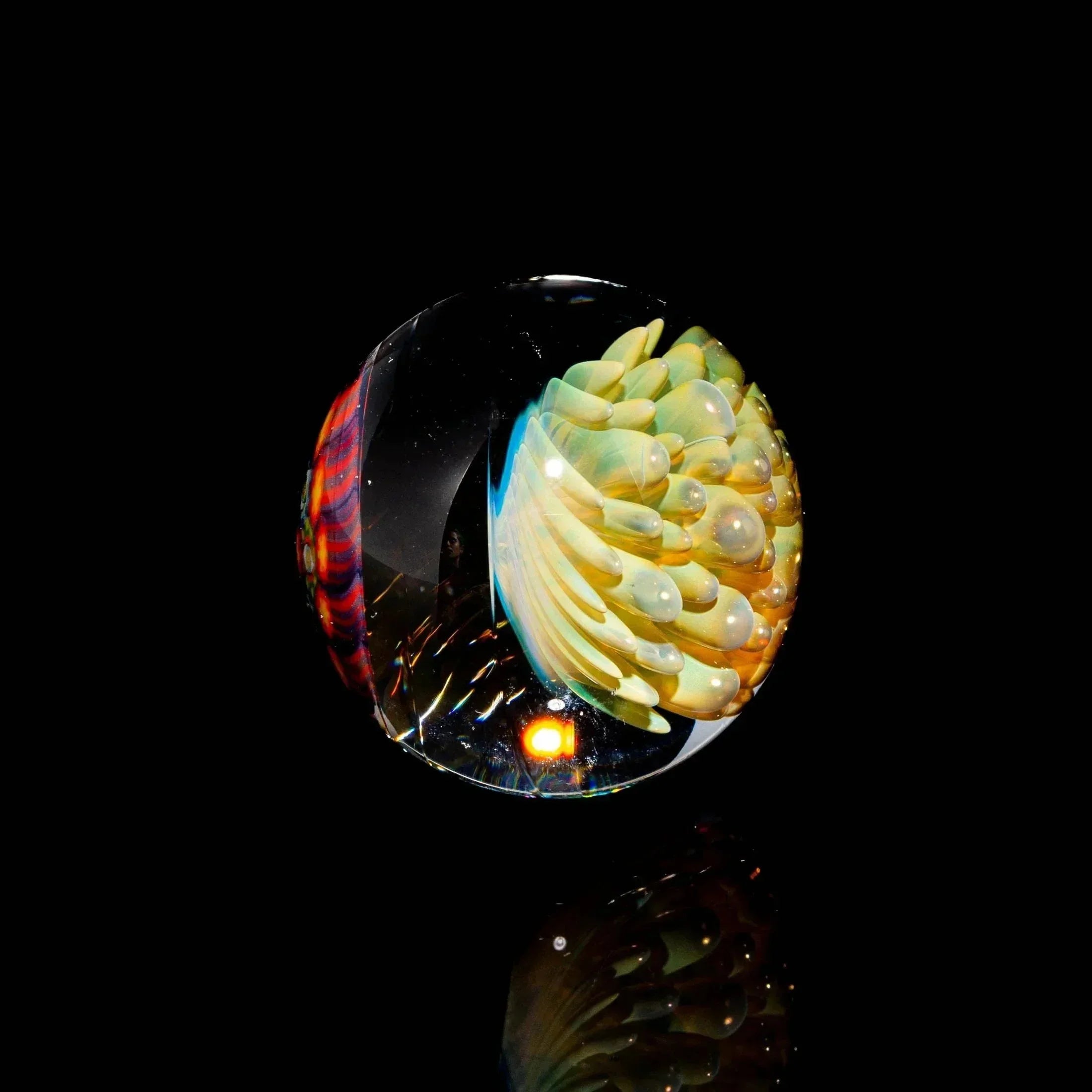 Handcrafted glass marble with intricate yellow and red patterns on a black background