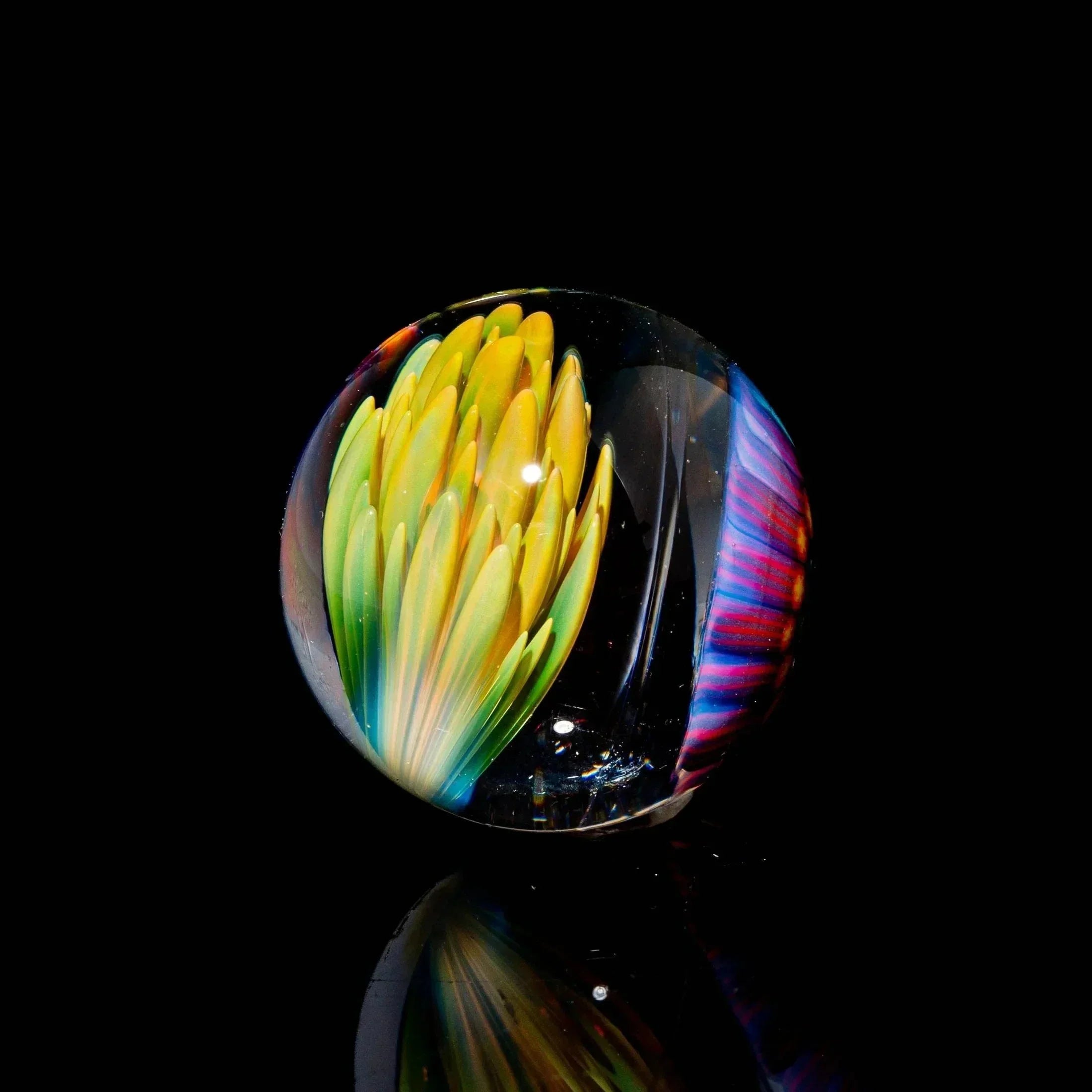 Handcrafted glass marble with yellow flower and rainbow accents on black background