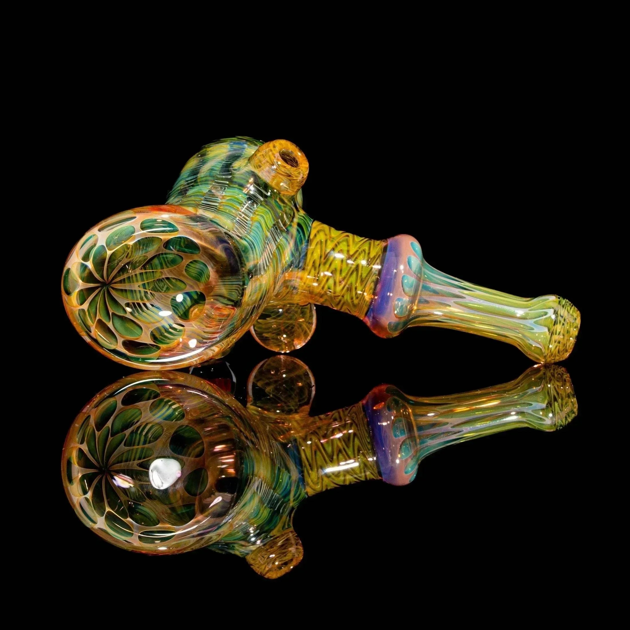 Colorful heady glass hand pipe with intricate patterns displayed on a reflective black surface.