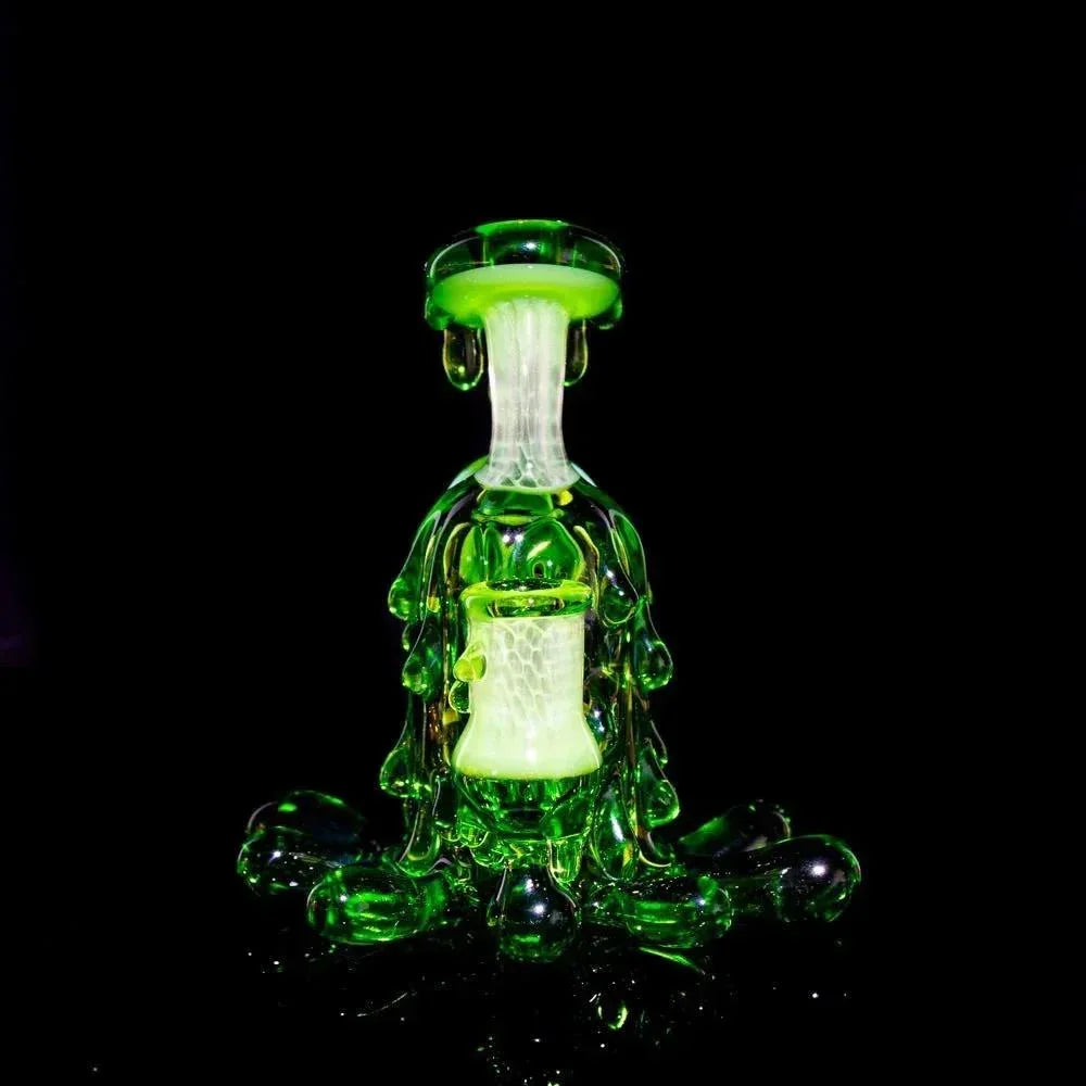 Green glass mini rig with unique splatter design, displayed on a black background.